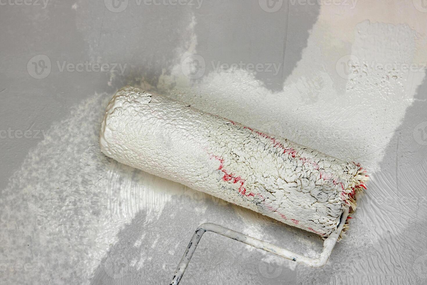 Creative graphic concept of paint roller applying fresh white paint onto the gray color concrete wall. Process of home renovation, improvement and makeover. Copy space. photo