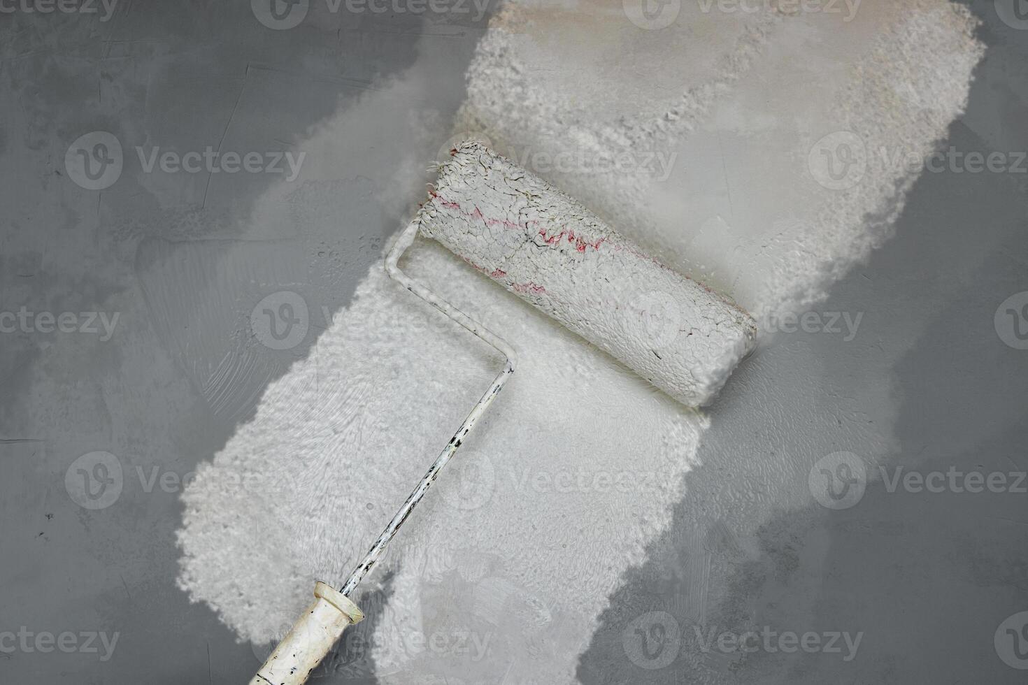 Creative graphic concept of paint roller applying fresh white paint onto the gray color concrete wall. Process of home renovation, improvement and makeover. Copy space. photo