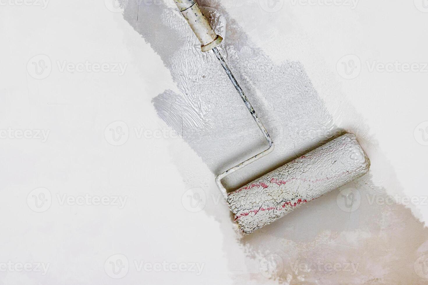 Creative graphic concept of paint roller applying fresh gray color paint onto the white concrete wall. Process of home renovation, improvement and makeover. Copy space. photo