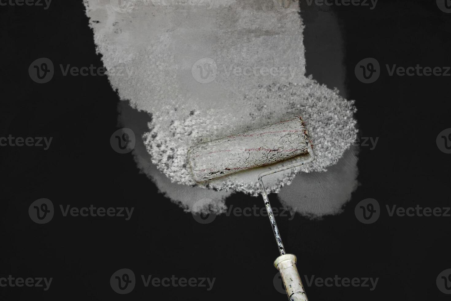 Creative graphic concept of paint roller applying fresh white paint onto the black color concrete wall. Process of home renovation, improvement and makeover. Copy space. photo