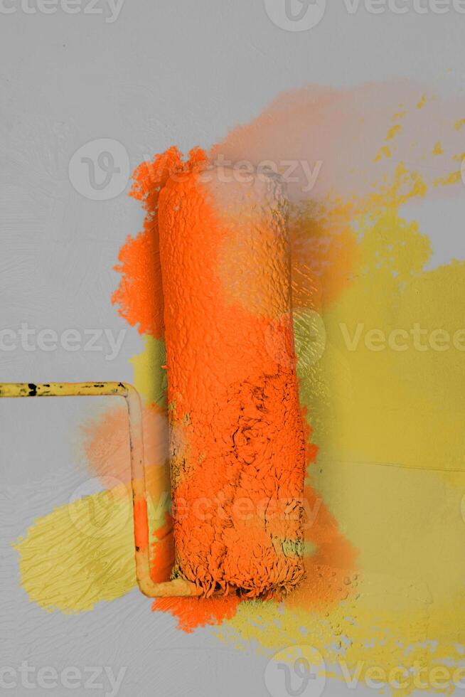 Creative graphic concept of paint roller applying fresh orange yellow color paint onto the gray white concrete wall. Process of home renovation, improvement and makeover. Copy space. photo