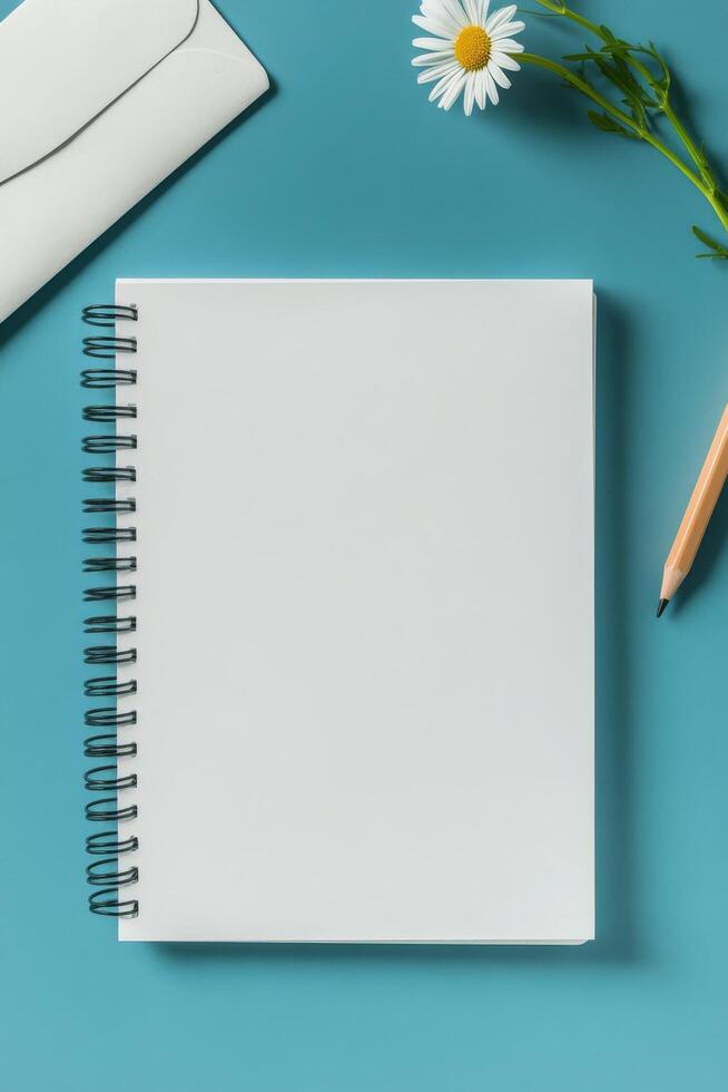 A blank notebook, pencil, flowers, and an envelope positioned on a blue background photo