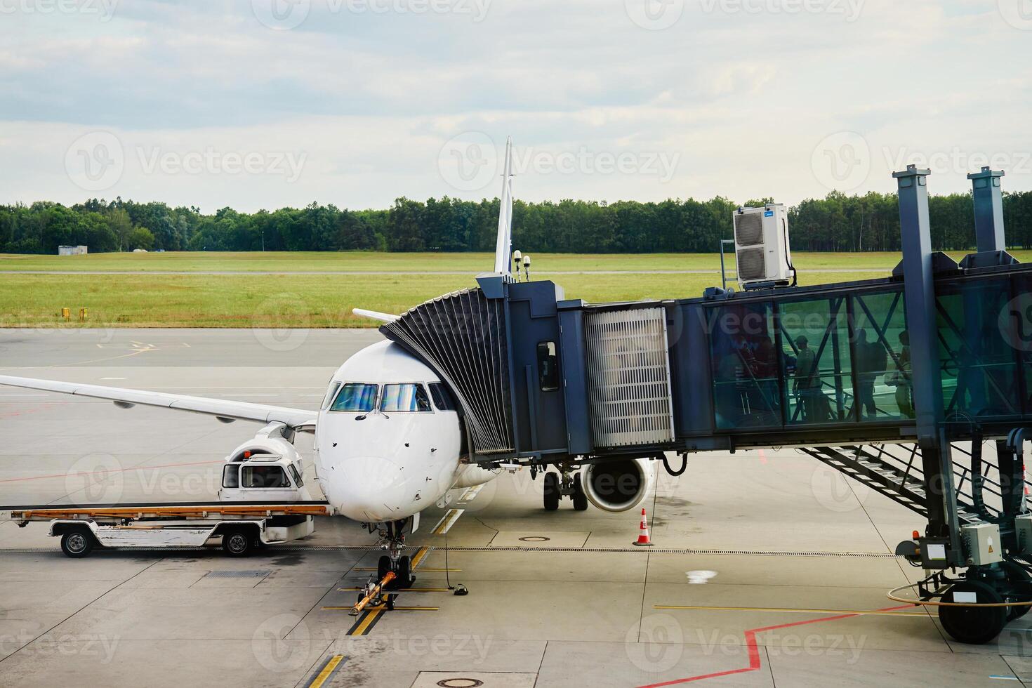 Passenger airplane docked at airport gate with connected jet bridge and ground support vehicle. Passengers boarding white airplane photo
