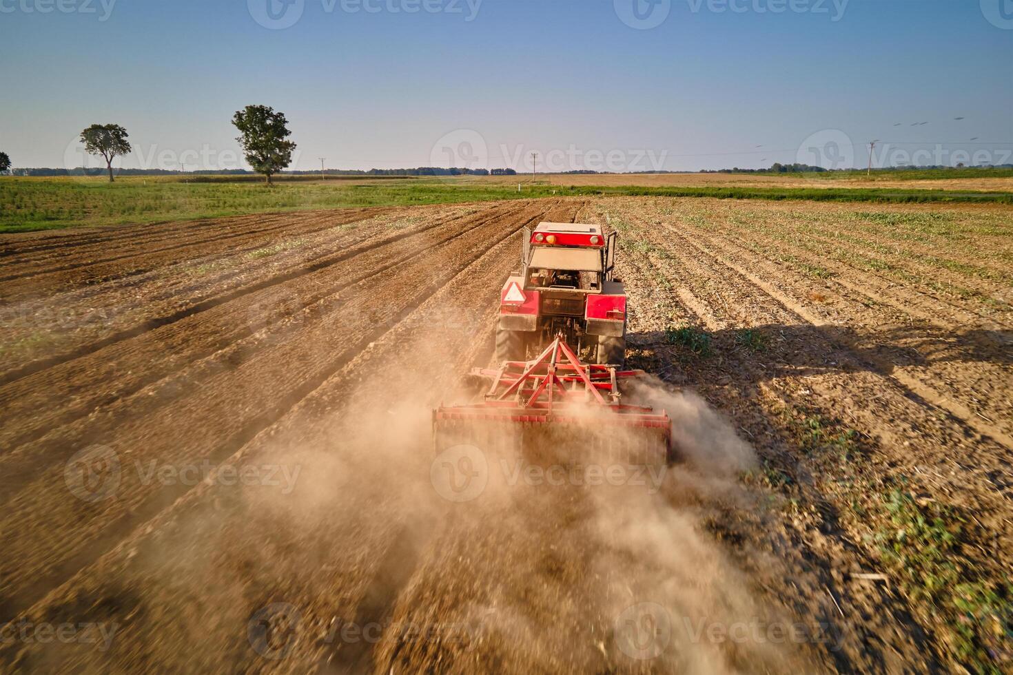 Red tractor working in agricultural field, cultivating and plowing dry soil, aerial view. Agribusiness concept. Small farming concept photo
