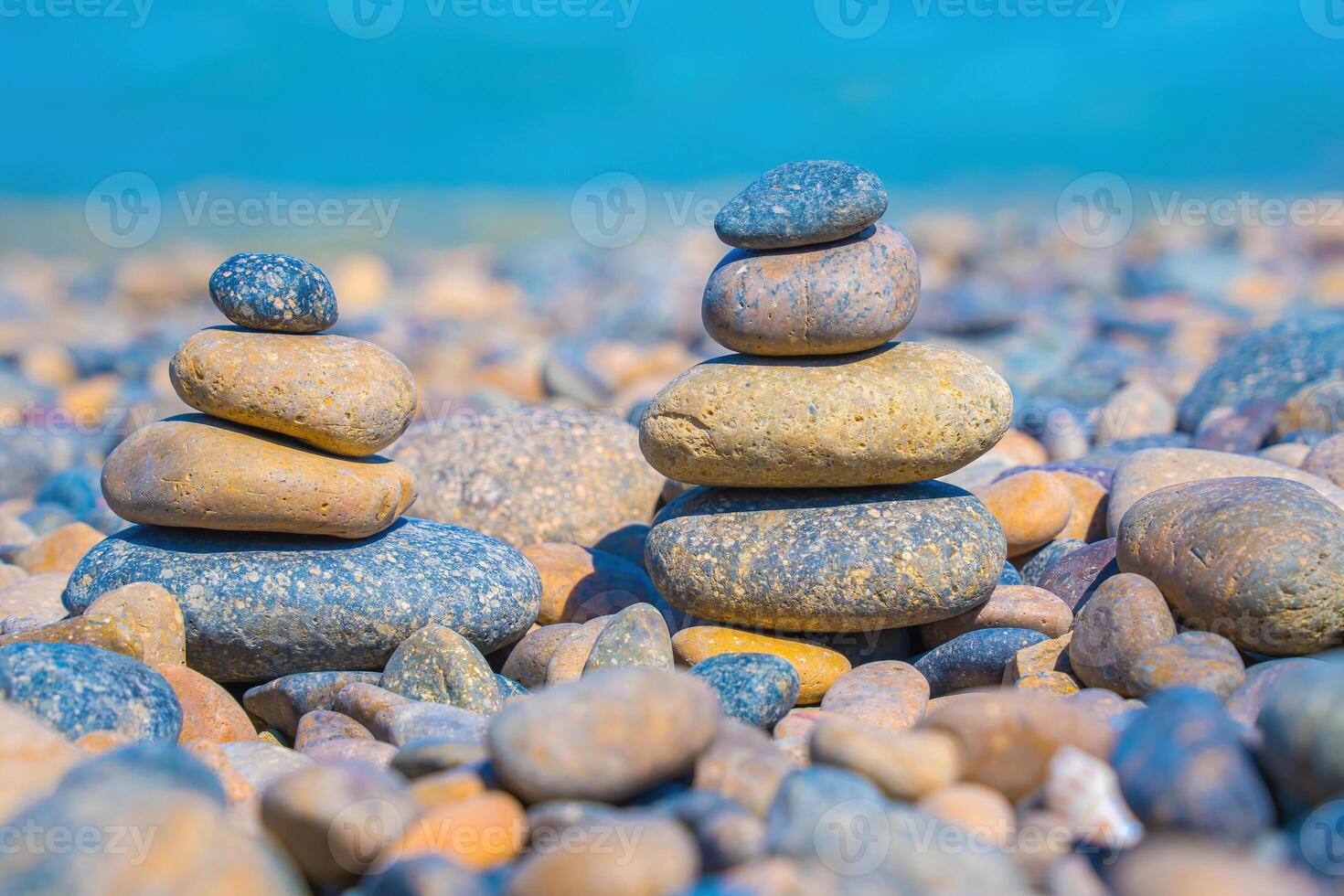 Symbolic scales of stones against the background of the sea and blue sky. Concept of harmony and balance. Pros and cons concept. Pyramid stones balance on the sand of the beach with blurred background photo