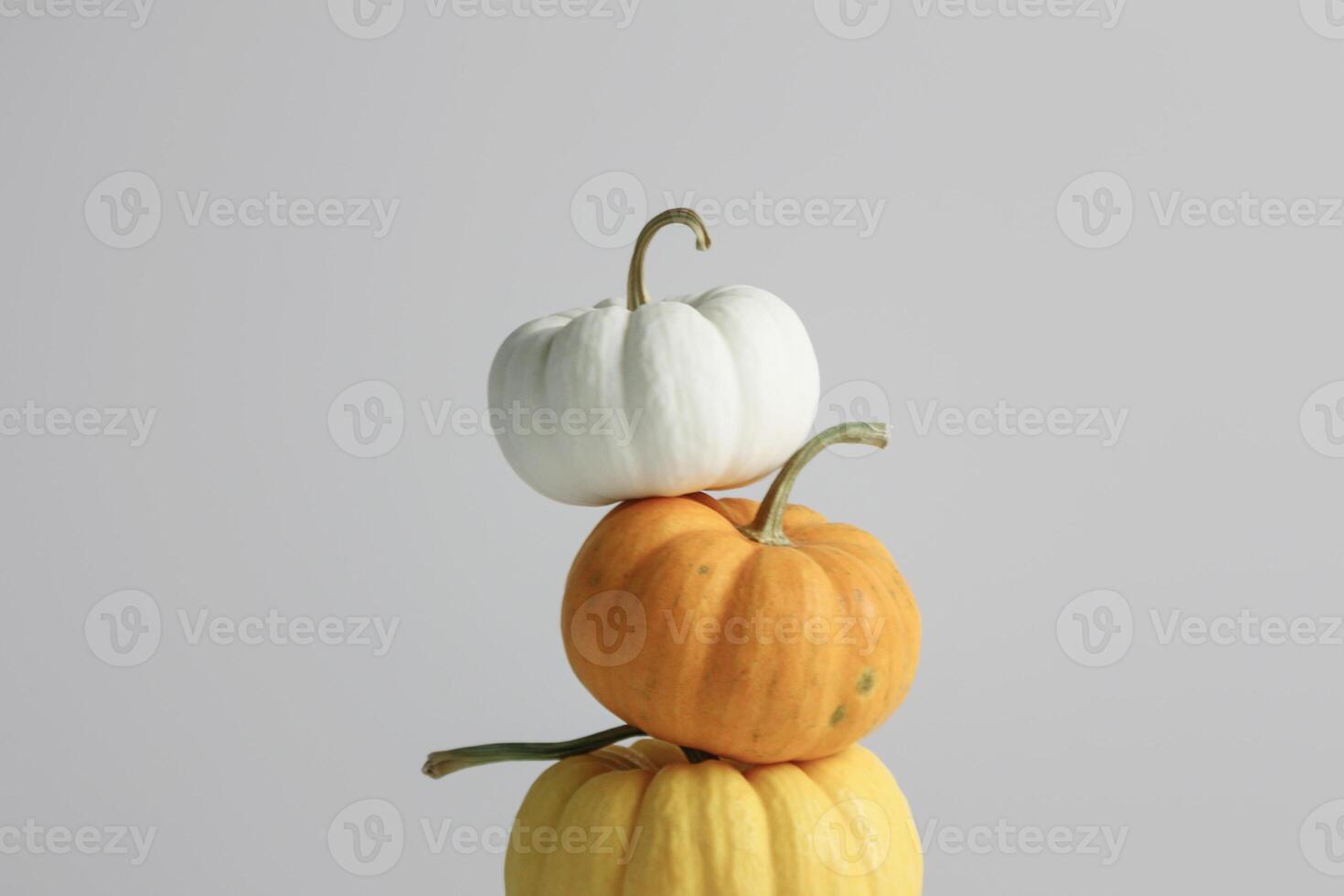 A stack of three decorative pumpkins in white, orange, and yellow against a neutral background photo