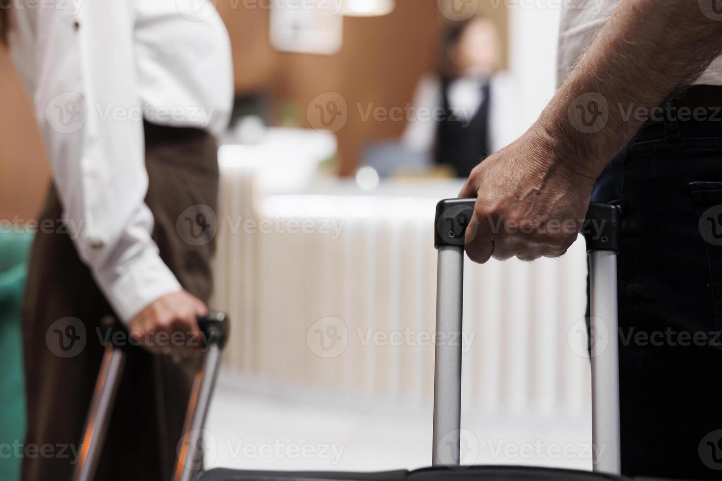 Close-up of a caucasian couple with bags entering foyer of a luxury hotel. View of retired senior customers holding bags as they approach the registration counter to check in with receptionists. photo