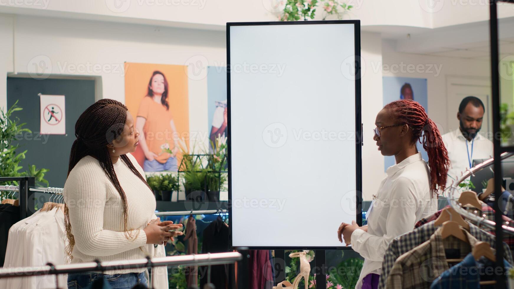 African american shopkeeper in clothing store using augmented reality screen to show woman garment options for her to pick. Clerk assistant using led display to help customer visualize fashion choices photo