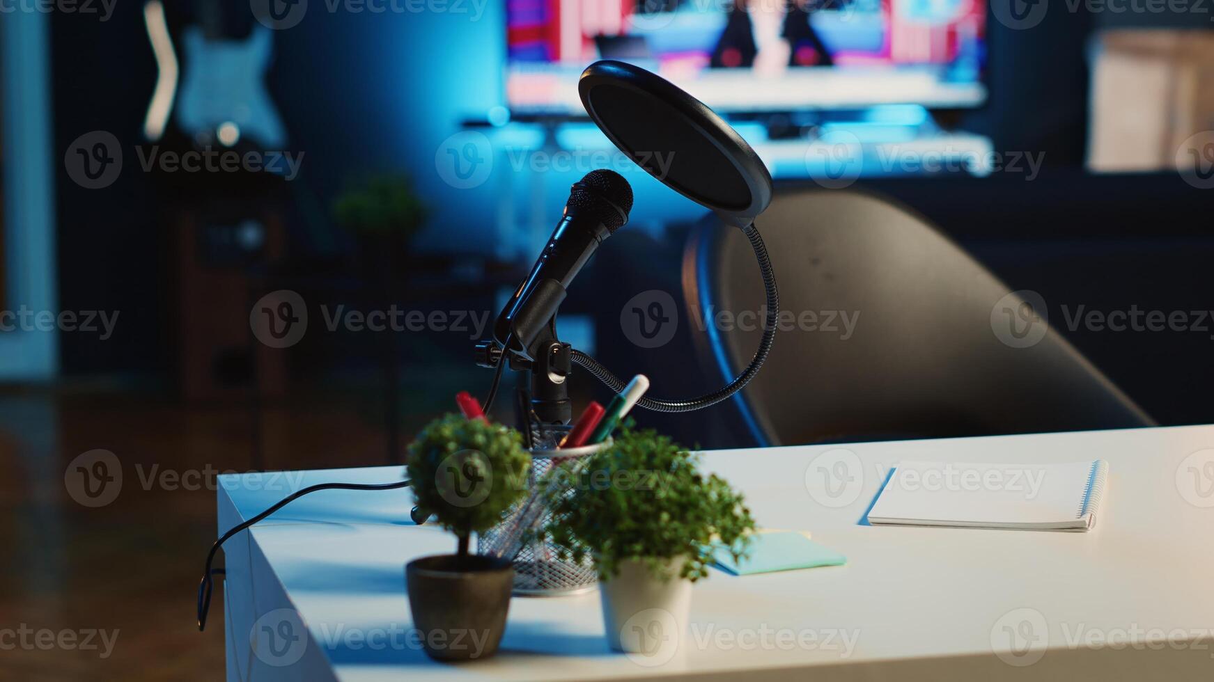 Panning shot of coffee table with microphone and mini house plants in dimly lit empty home studio interior. Podcast recording equipment in apartment illuminated by RGB lights, close up photo
