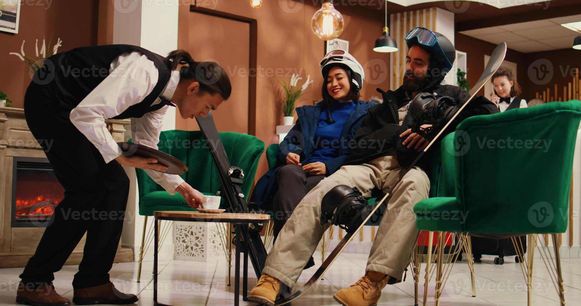 Man paying for refreshment with card and tips, using pos to buy hot coffee drink and give cash to bellhop in lounge area. Couple waiting to go snowboarding on alpine slopes. Tripod shot. photo