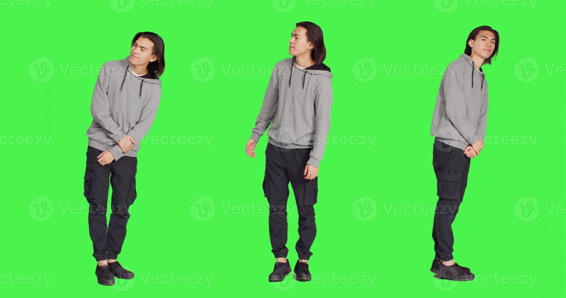 In studio, young guy poses against greenscreen, looking at wristwatch and appearing distressed. Unhappy and irritated asian person is impatiently awaiting for stuff on camera. photo