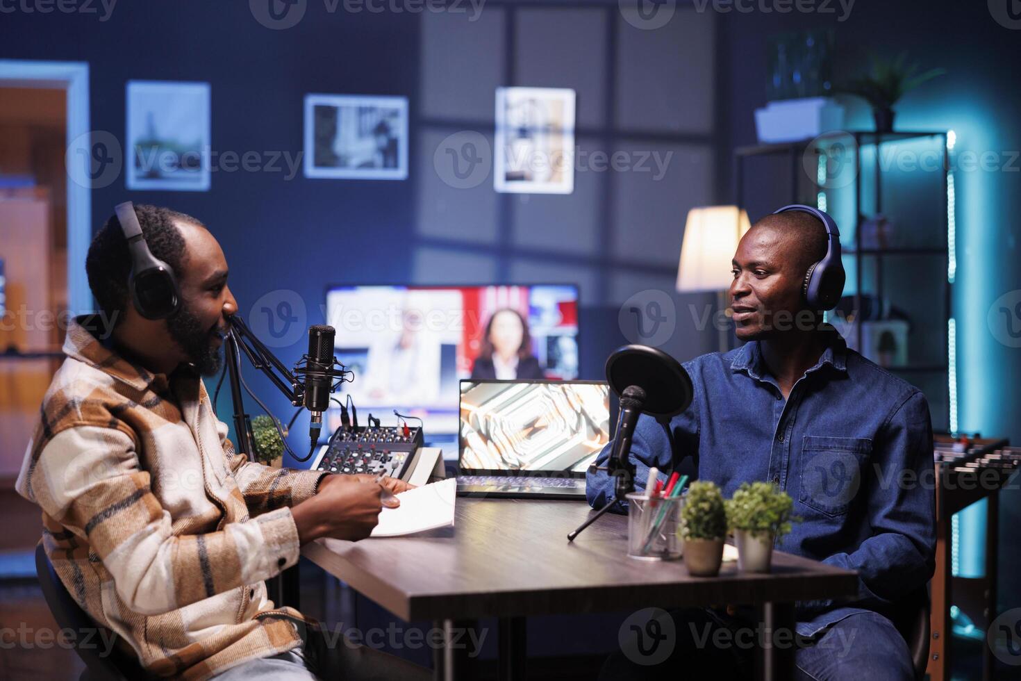 Black man with notebook is interviewing social media star and using audio equipment to record the program. Online radio host casually talking with influencer in home studio, recording podcast episode. photo