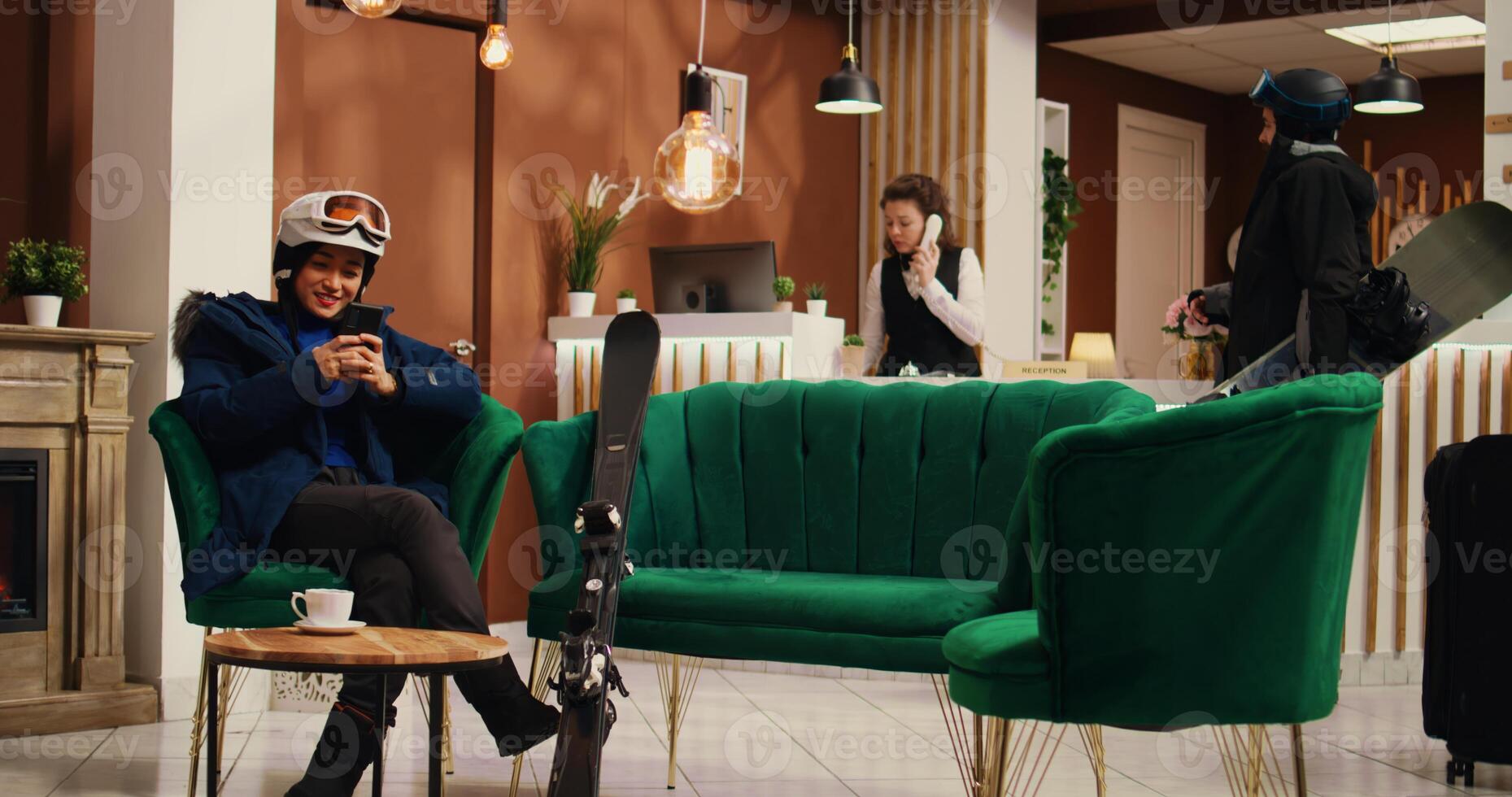 Asian tourist messaging on smartphone, asking friends to meet skiing on alpine slopes at mountain lodging complex. Winter sport fan checking phone and social media page before sliding down. photo