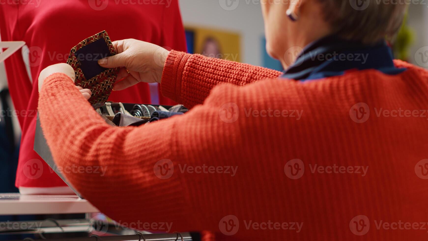 Elderly woman browsing through clothes in Christmas decorated shopping store, trying to pick perfect necktie for husband as xmas present during winter holiday season, close up photo