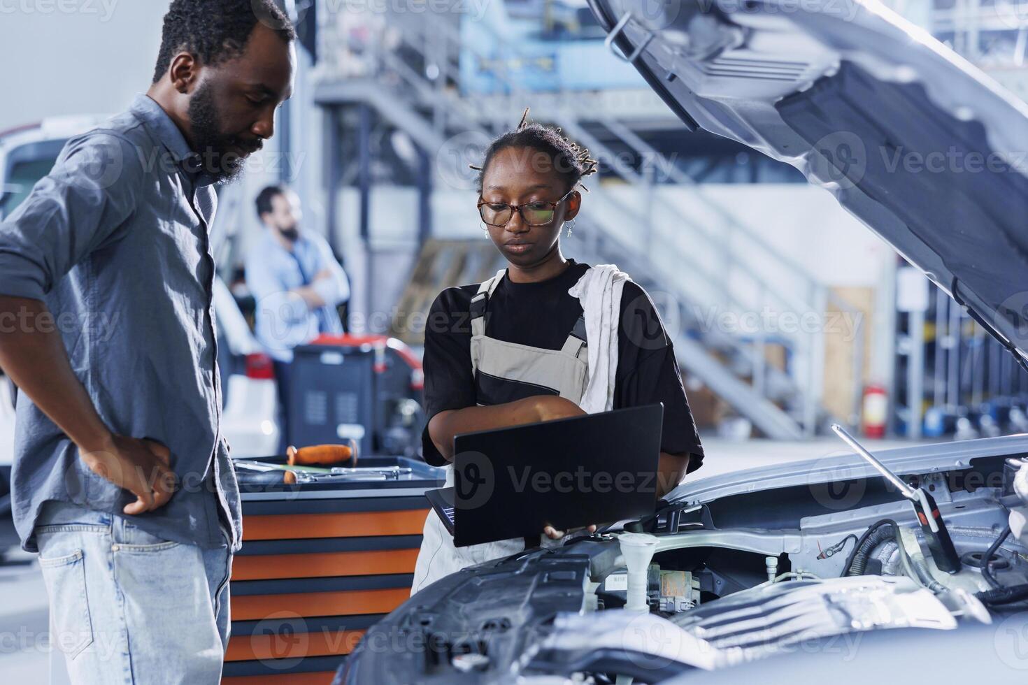 Technician in car service uses laptop to calculate invoice after fixing broken automobile engine. Diligent garage employee uses device to inform client of final costs after mending vehicle photo