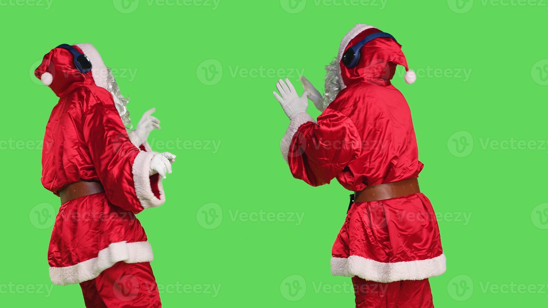 Joyful santa dancing on songs in studio, using headset to listen music and spread positivity during christmas holiday. Person dressed like saint nick showing cool dance moves, greenscreen. photo