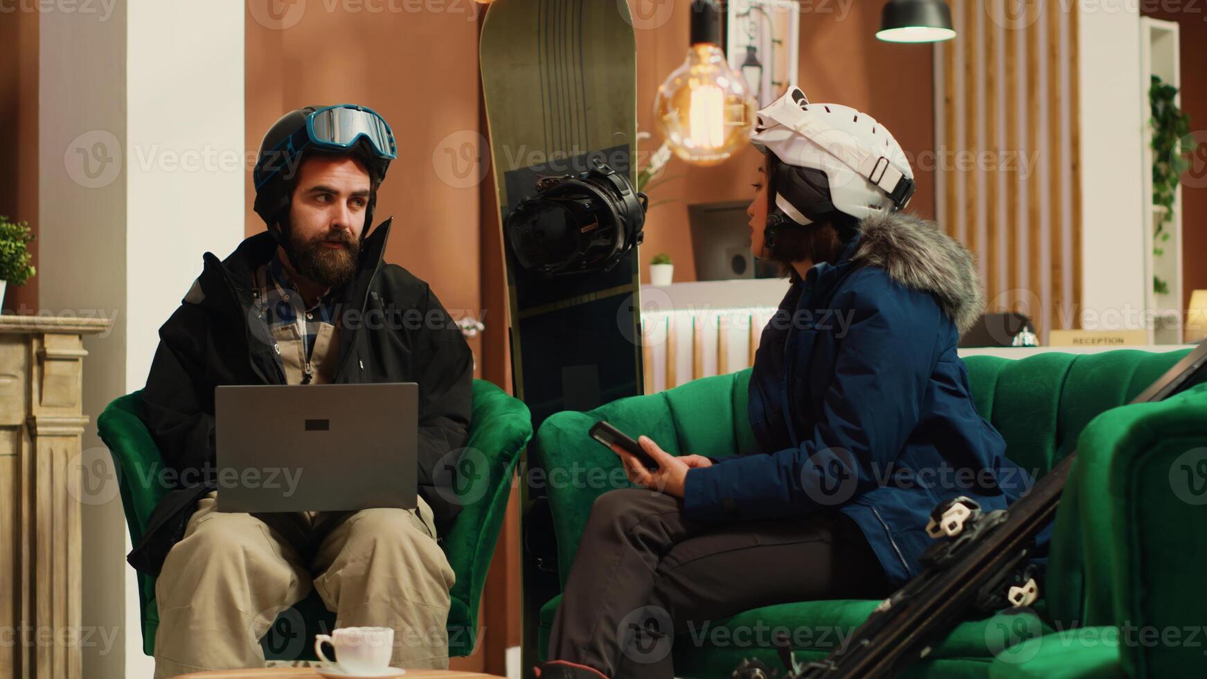 Focused people using devices in lobby, arriving at ski resort during wintertime. Man searches for slopes activity information online while woman checks text messages or social media. Handheld shot. photo