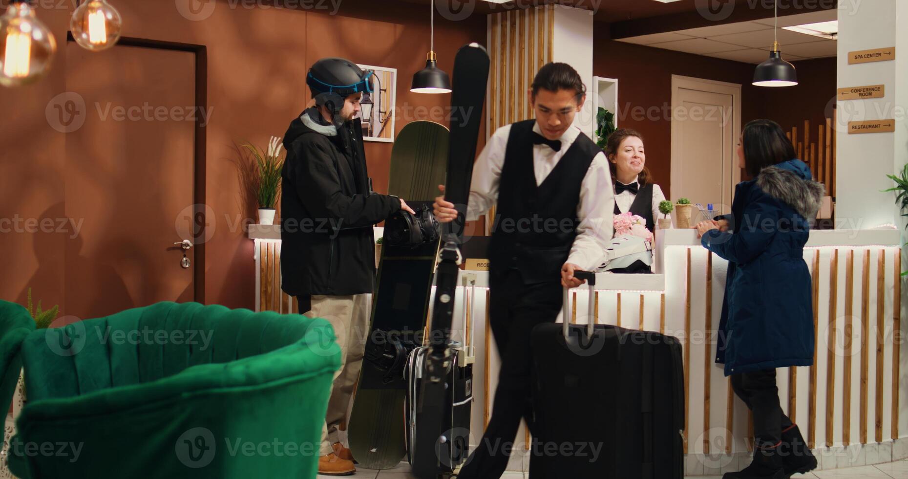 Athletic partners in winter apparel stand at hotel front desk during vacation, receptionists welcoming customers. Tourists with skiing and snowboarding tools ready for alpine adventures at resort. photo