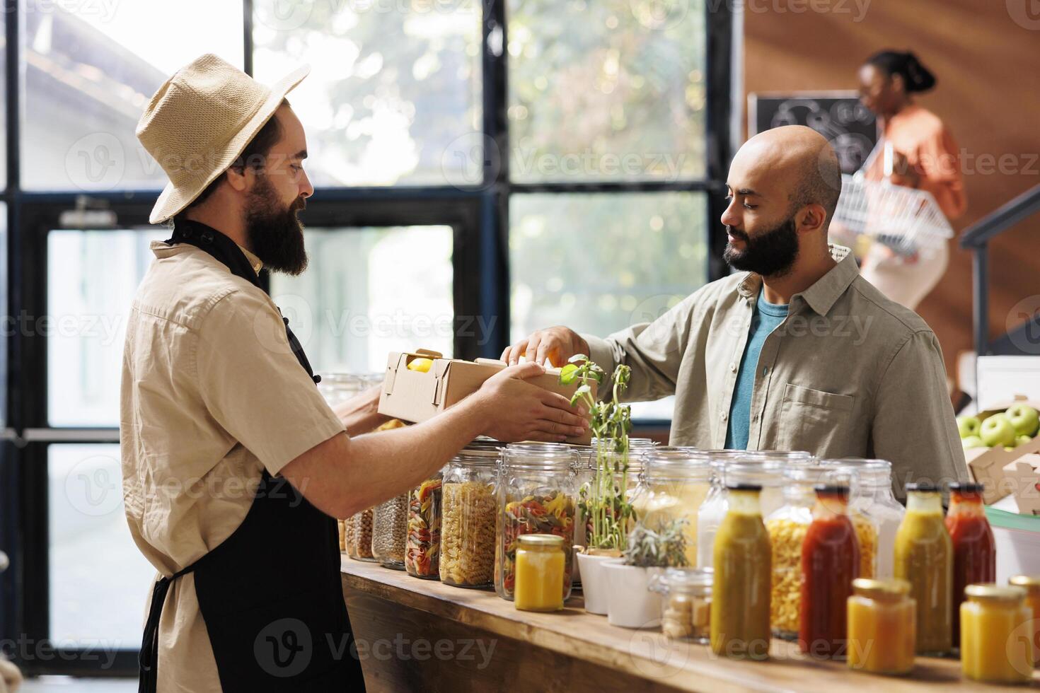 Caucasian male vendor showing freshly harvested box of fruits to the middle eastern client in eco friendly store. Shopkeeper with an apron carrying locally grown lemons to present to customer. photo