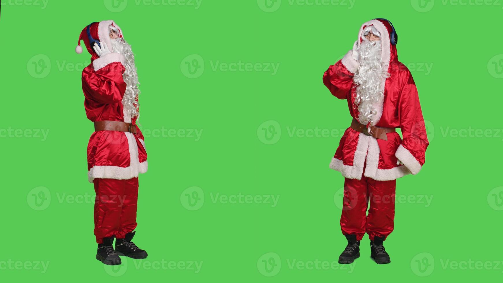 Saint nick having fun with music, listening songs on headphones and dancing in red festive suit. Young man enjoying christmas eve celebration, using audio headset on greenscreen. photo