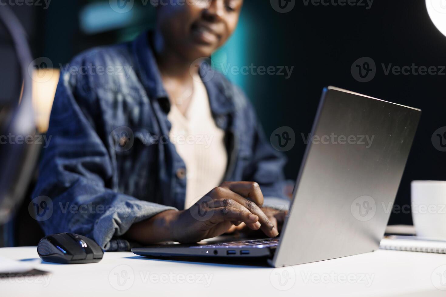 Close up of black woman at the desk typing on her personal computer, browsing the internet. African american freelancer using the laptop, answering emails, and working from home. photo