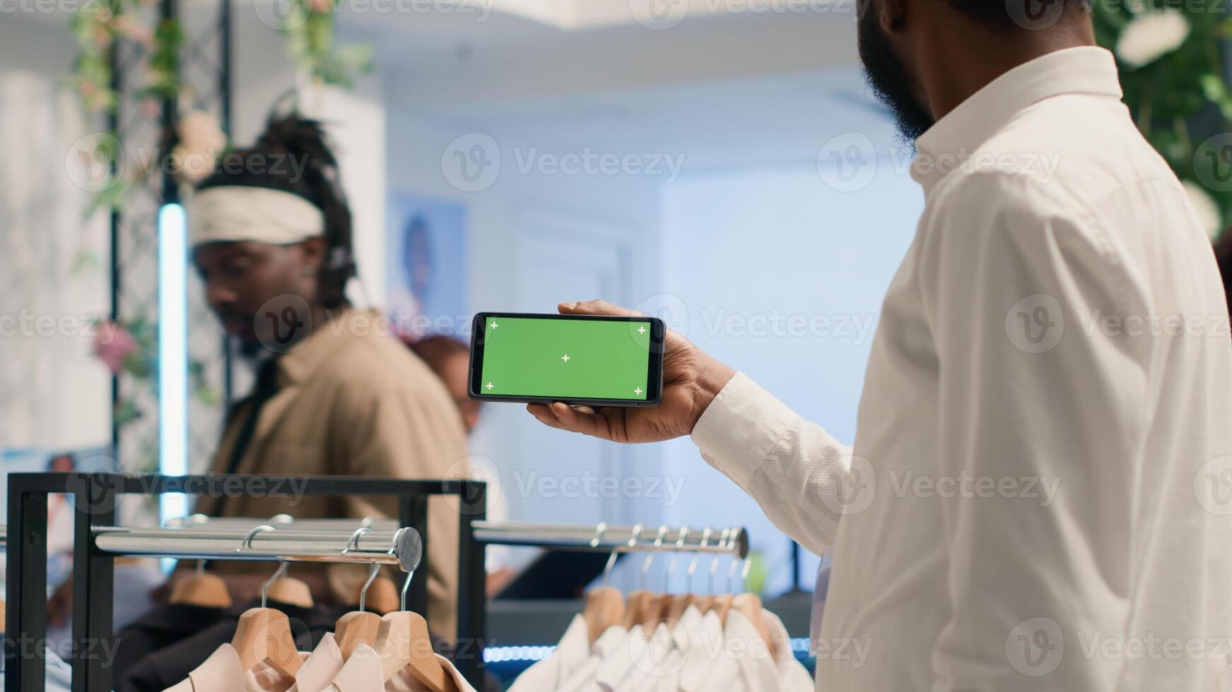 African american man holding green screen cellphone in luxury clothing shop with elegant formalwear shirts. BIPOC customer with chroma key mobile phone in fashion boutique photo