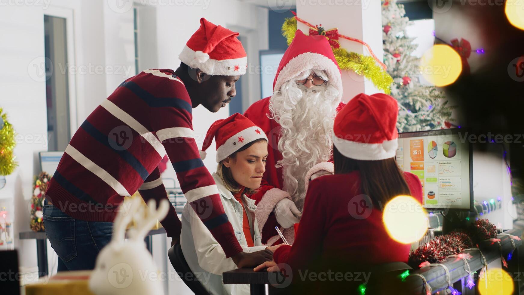 Team leader dressed as Santa during Christmas season delegates project tasks to workers. Director in xmas decorated workspace discussing with employees during winter holiday season photo