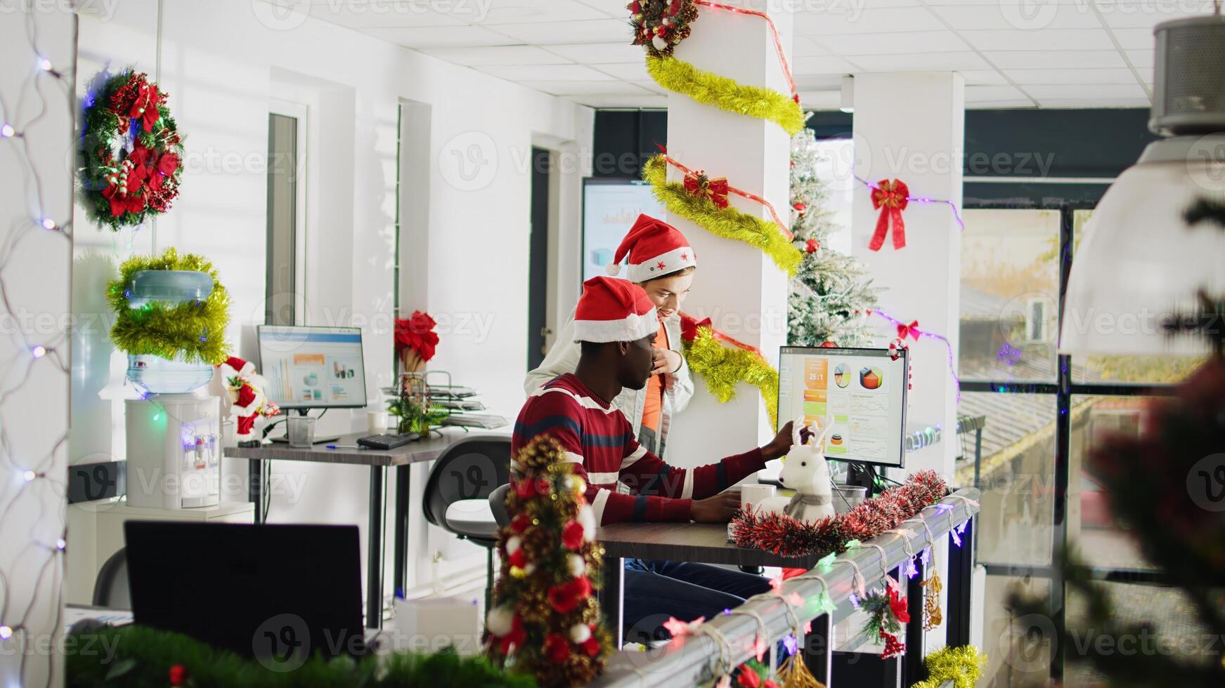 Zoom out shot of coworkers brainstorming ideas for project during Christmas season in festive ornate office. Workers in multicultural workplace adorn with xmas tree and wreaths photo