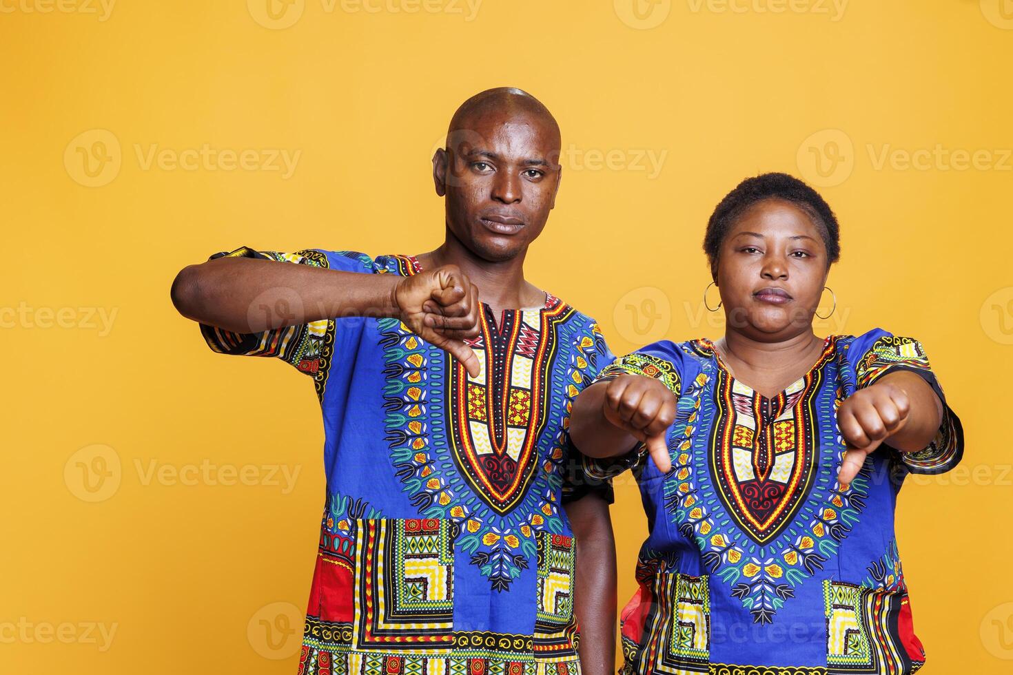 Man and woman standing with thumbs down gesture and looking at camera with serious expression. Confident mid adult black couple showing dislike and disagreement sign portrait photo