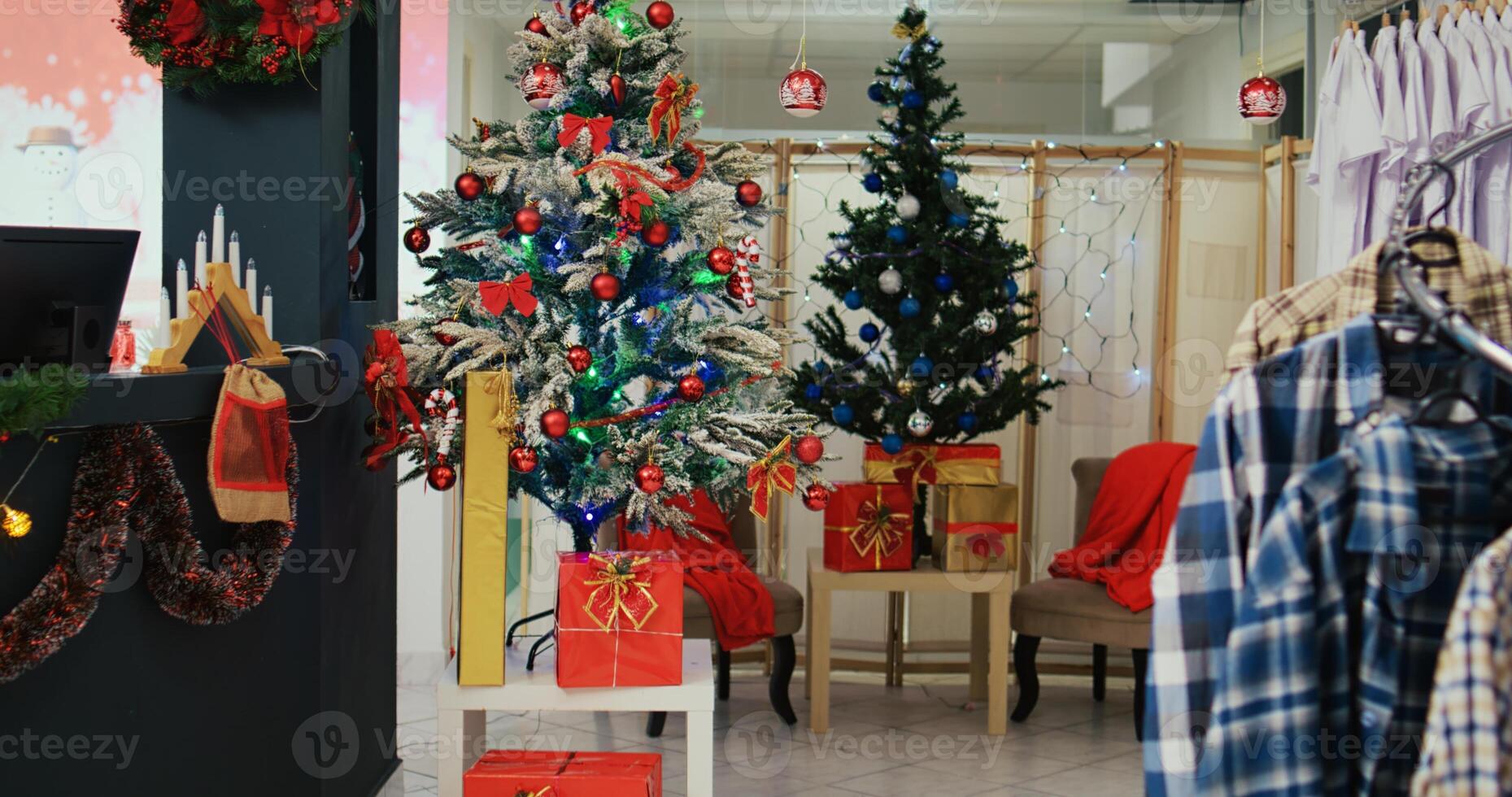 Dolly in shot of festive clothing store filled with beautifully decorated Christmas trees, garlands and ornaments during winter holiday season. Empty fashion boutique with clothes on racks photo