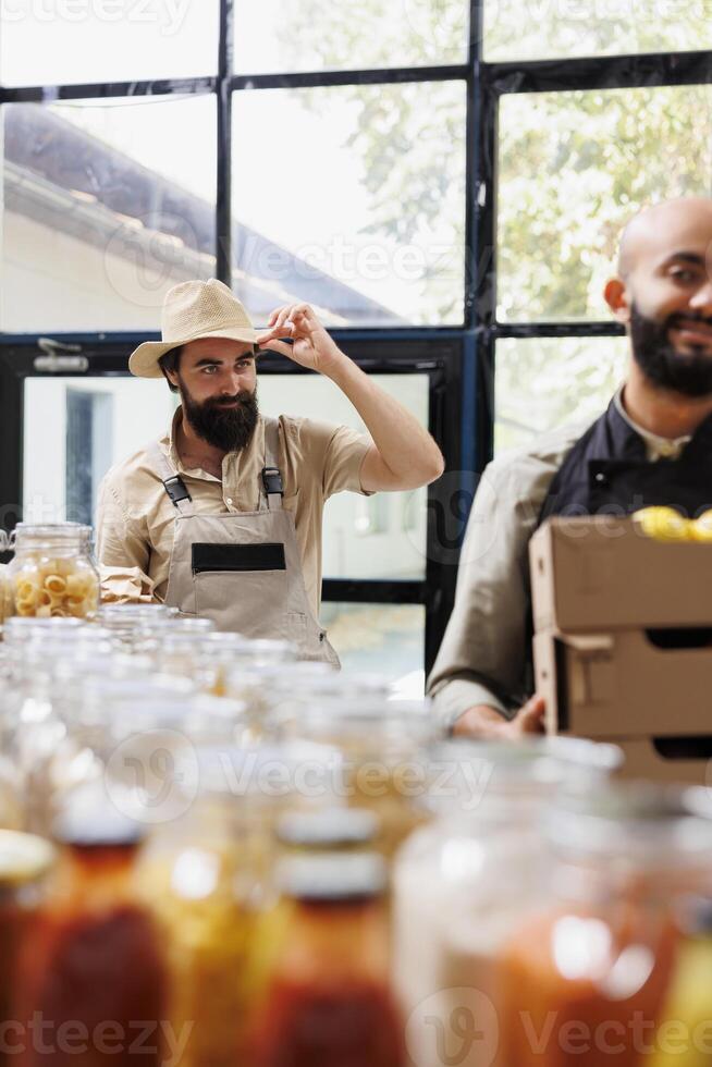 Local farmer provides organic items to happy vendor who serves eco conscious customers in zero-waste store. Young man delivers crates full of freshly harvested, nutritious produce to retailer. photo