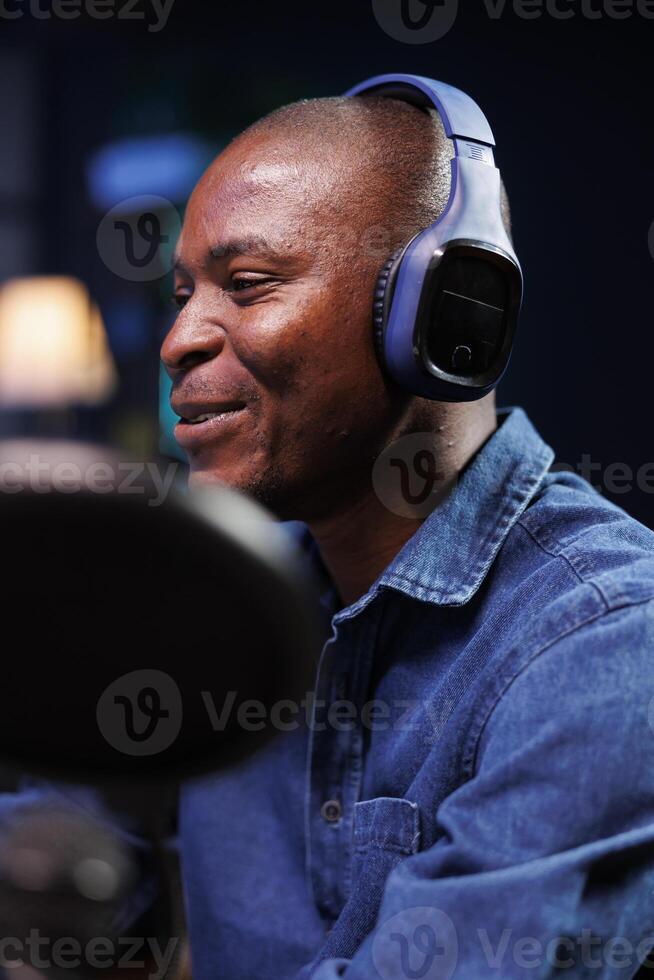 Selective focus of african american influencer utilizing professional audio equipment for making podcast episode. Closeup of smiling black man using wireless headset and microphone in his radio show. photo