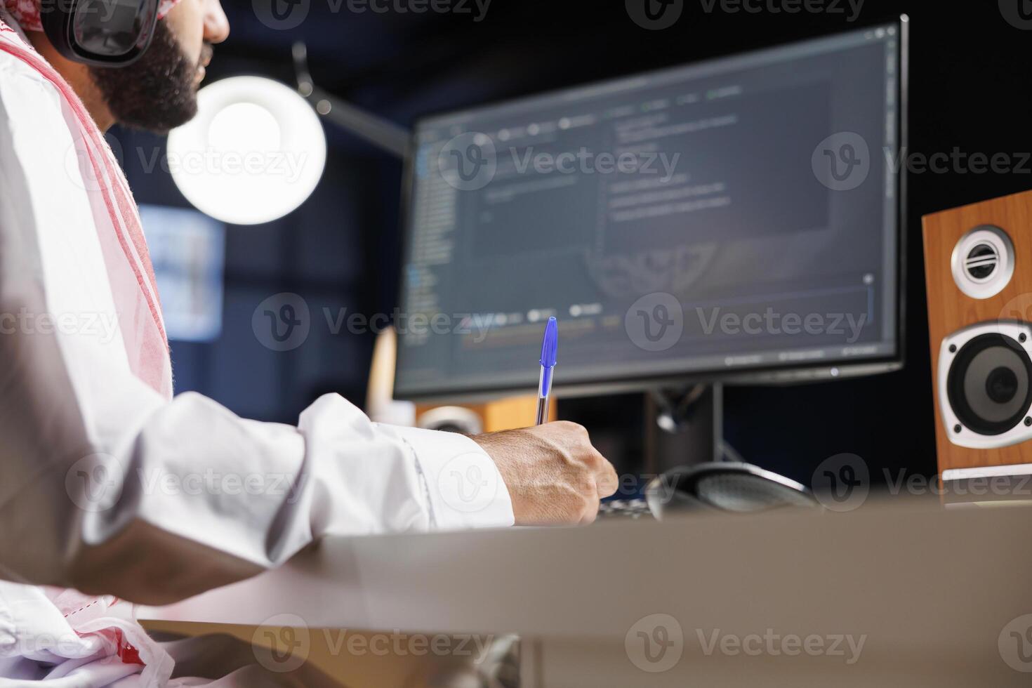 Middle Eastern software developer coding on a laptop to demonstrate the foundations of software development. While using wireless headphones, an Arab guy runs algorithms. Close-up shot. photo