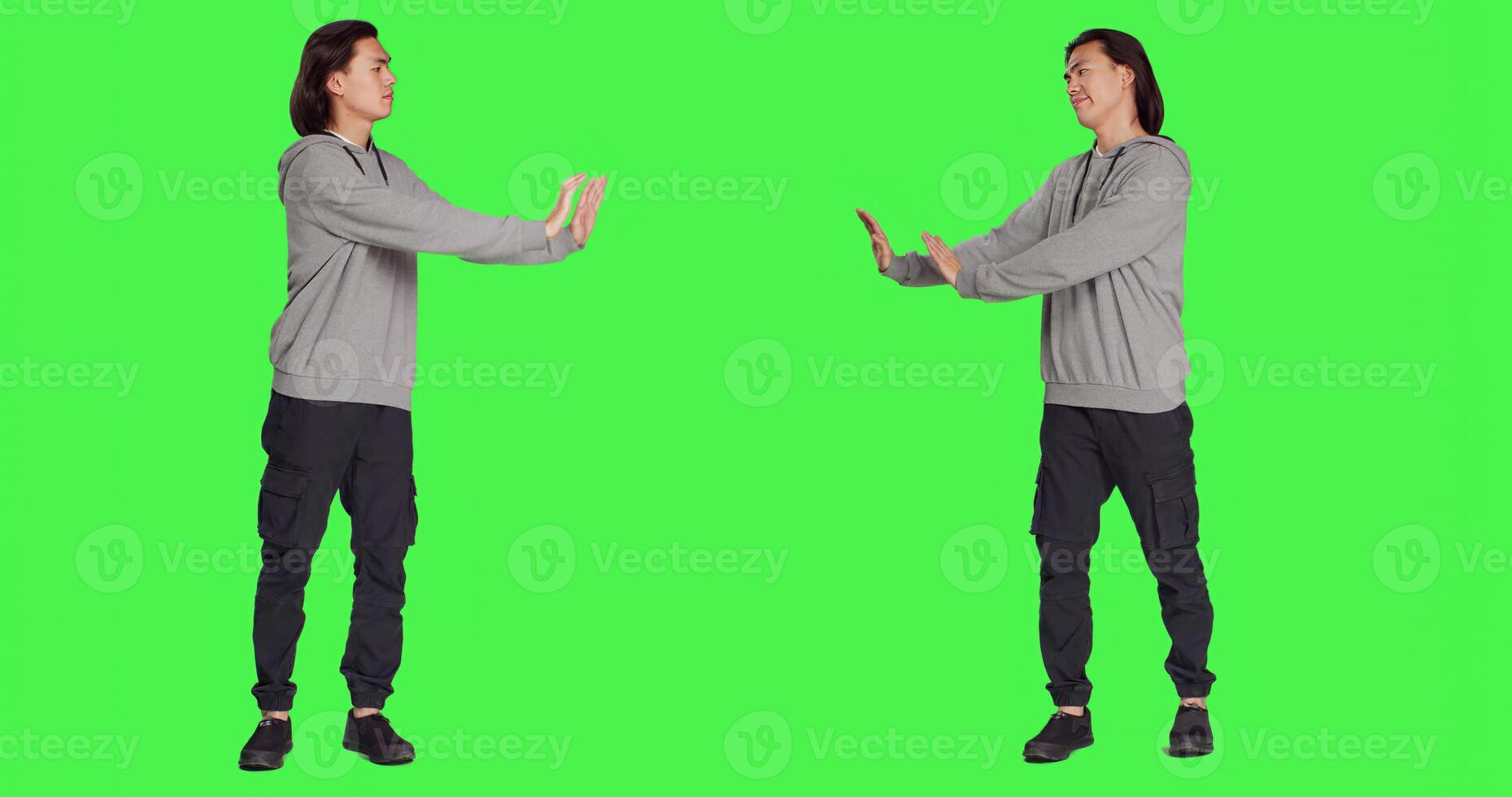 In studio, person tries to shove object aside, presenting rejection or resistance. Against isolated full body greenscreen set, young model resembles refusal and disagreement with stop gesture. photo