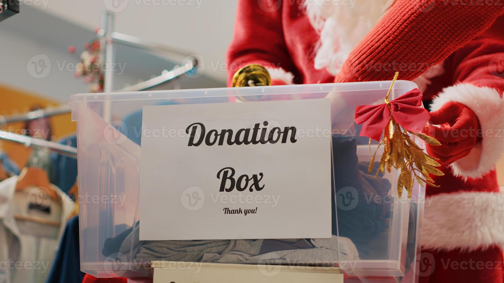 Close up shot of donation box in fashion shop set up for humanitarian help during Christmas holiday season. Worker dressed as Santa Claus collecting unneeded clothes from generous clients photo