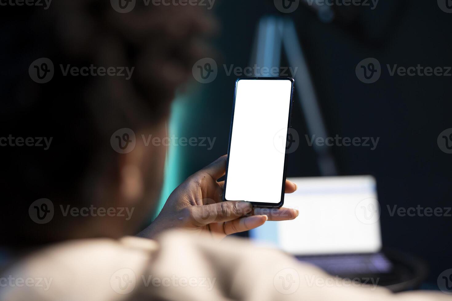 Cozy african american man chatting with online friends using mockup phone in warm stylish home, enjoying himself. Person scrolling on isolated screen cellphone entertained by social media activity photo
