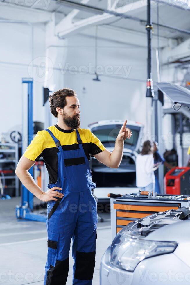 Repairman in repair shop using augmented reality holograms to check car blueprint during checkup. Hardworking garage employee using futuristic AR technology to examine malfunctioning vehicle photo