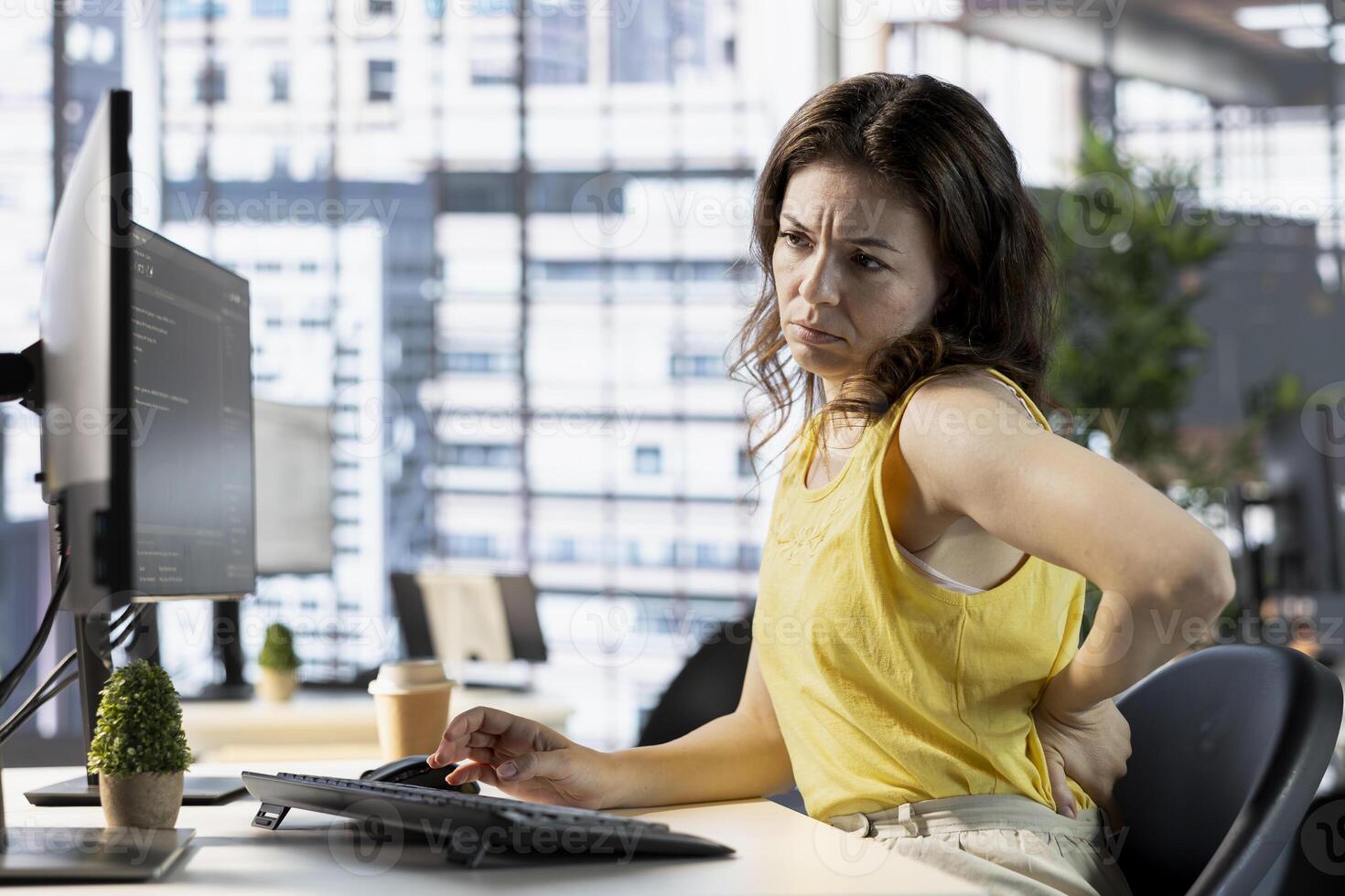 Programmer feeling back pain while sitting at desk testing company software to minimize occurrence of bugs. Fatigued woman suffering pain from incorrect posture while writing code photo