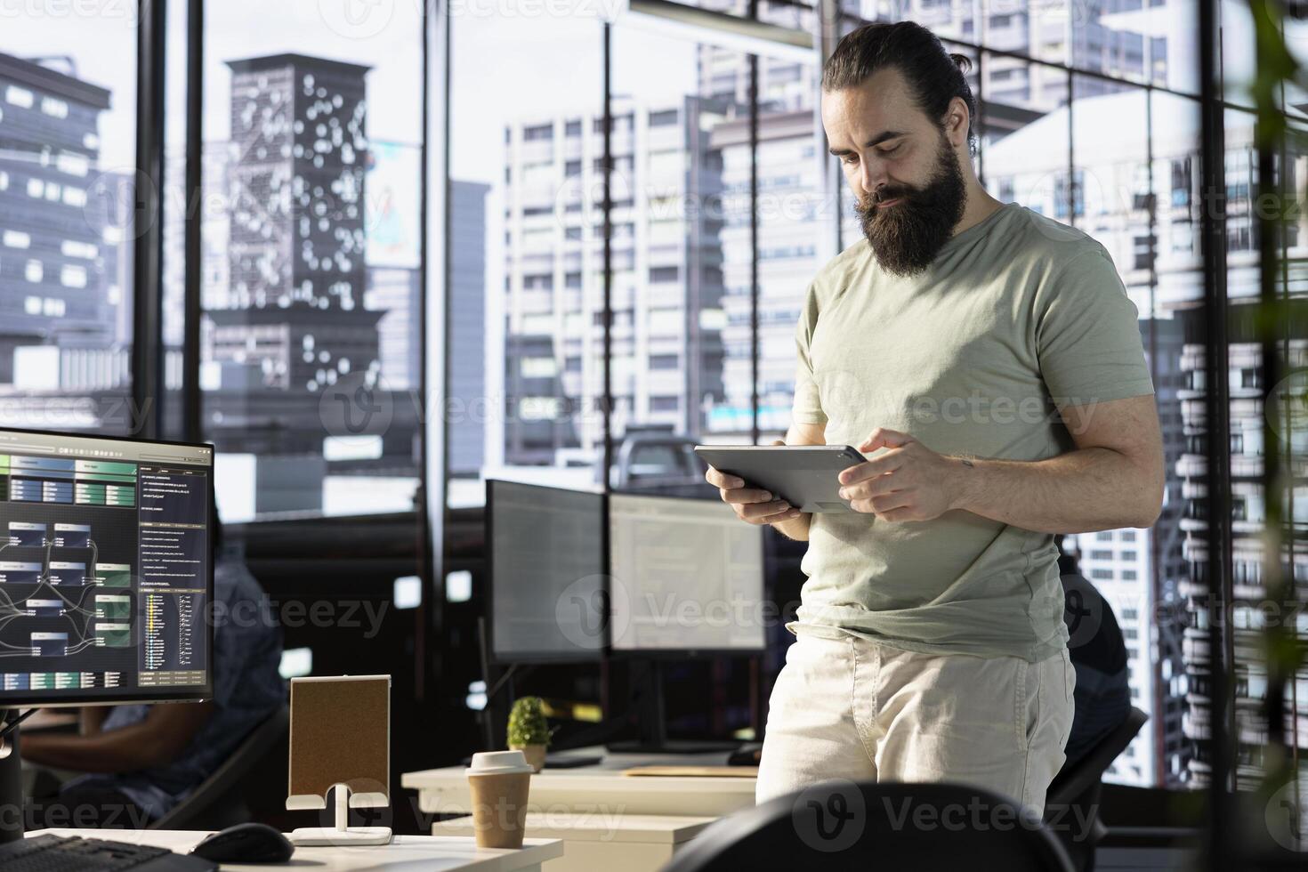 Programmer checking results on tablet after creating complex machine learning models that can process and analyze vast amounts of data. Man standing in office, looking at digital device photo