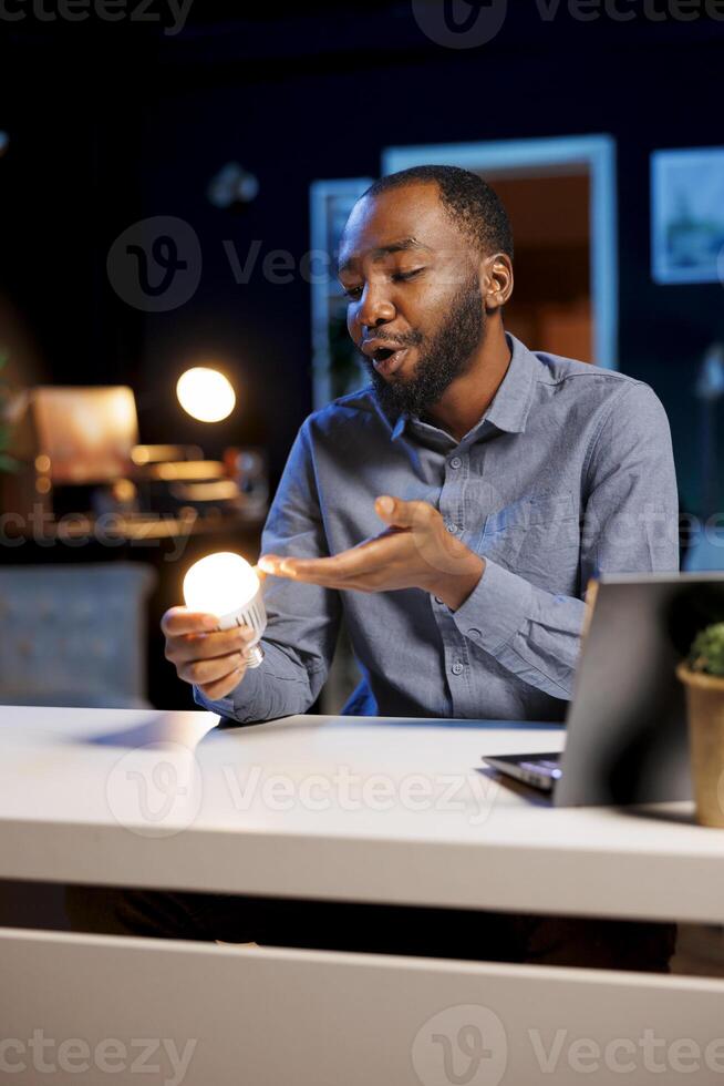 Content creator talking about house improvement topic, showing newly launched smart light bulb to subscribers. Tech guru presenting WIFI home automation device to fans photo