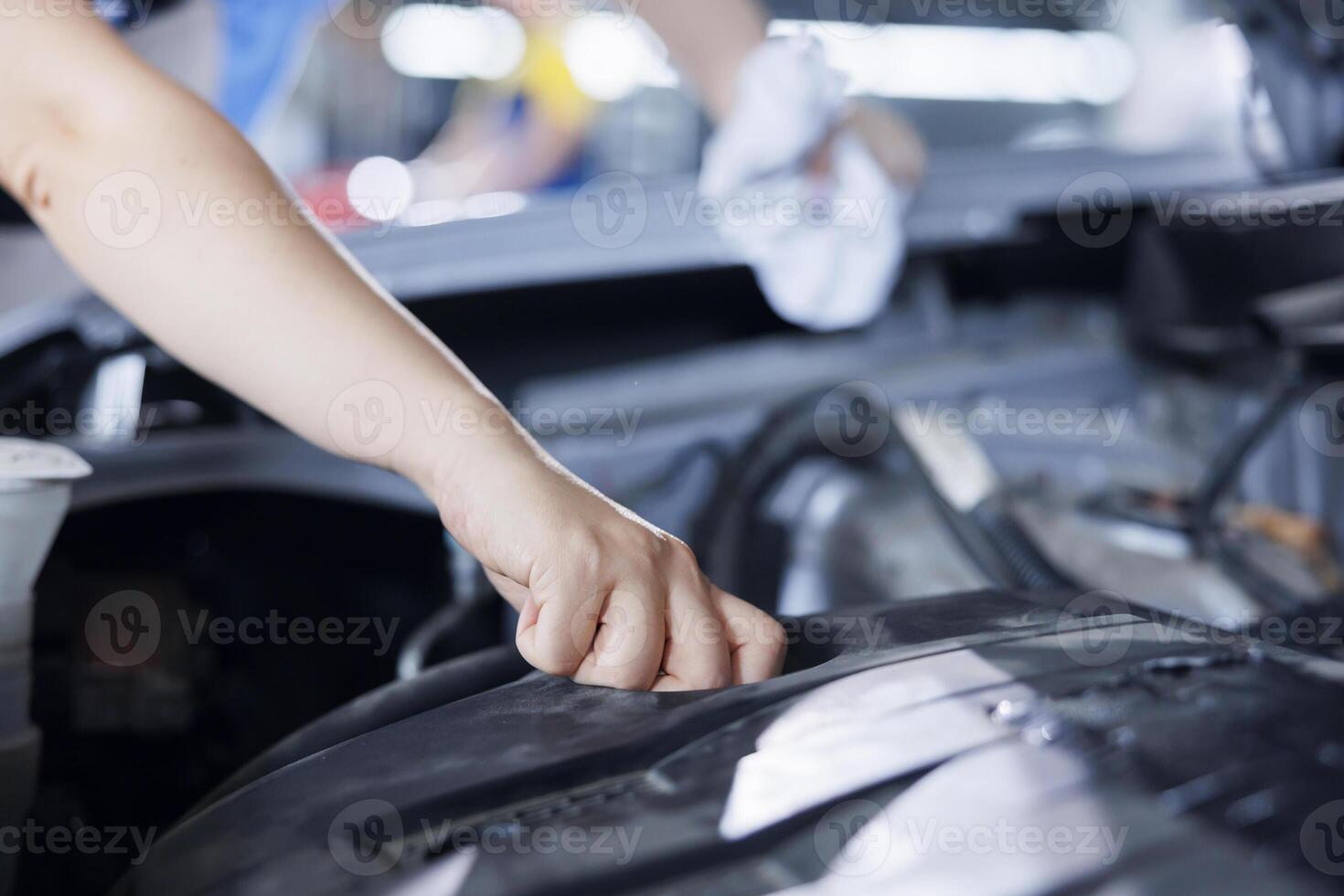 Precise serviceman in garage finishing fixing car, looking underneath vehicle hood to remove remaining oil leaks. Worker does routine alternator cleaning on client automobile in auto repair shop photo