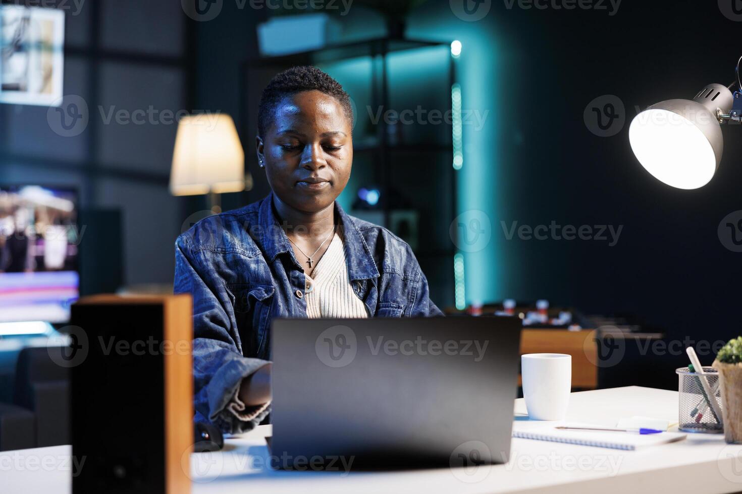 Young black woman sitting at desk and typing on digital laptop, replying to emails. African american female blogger working at home, utilizing her personal computer for writing online blogs. photo