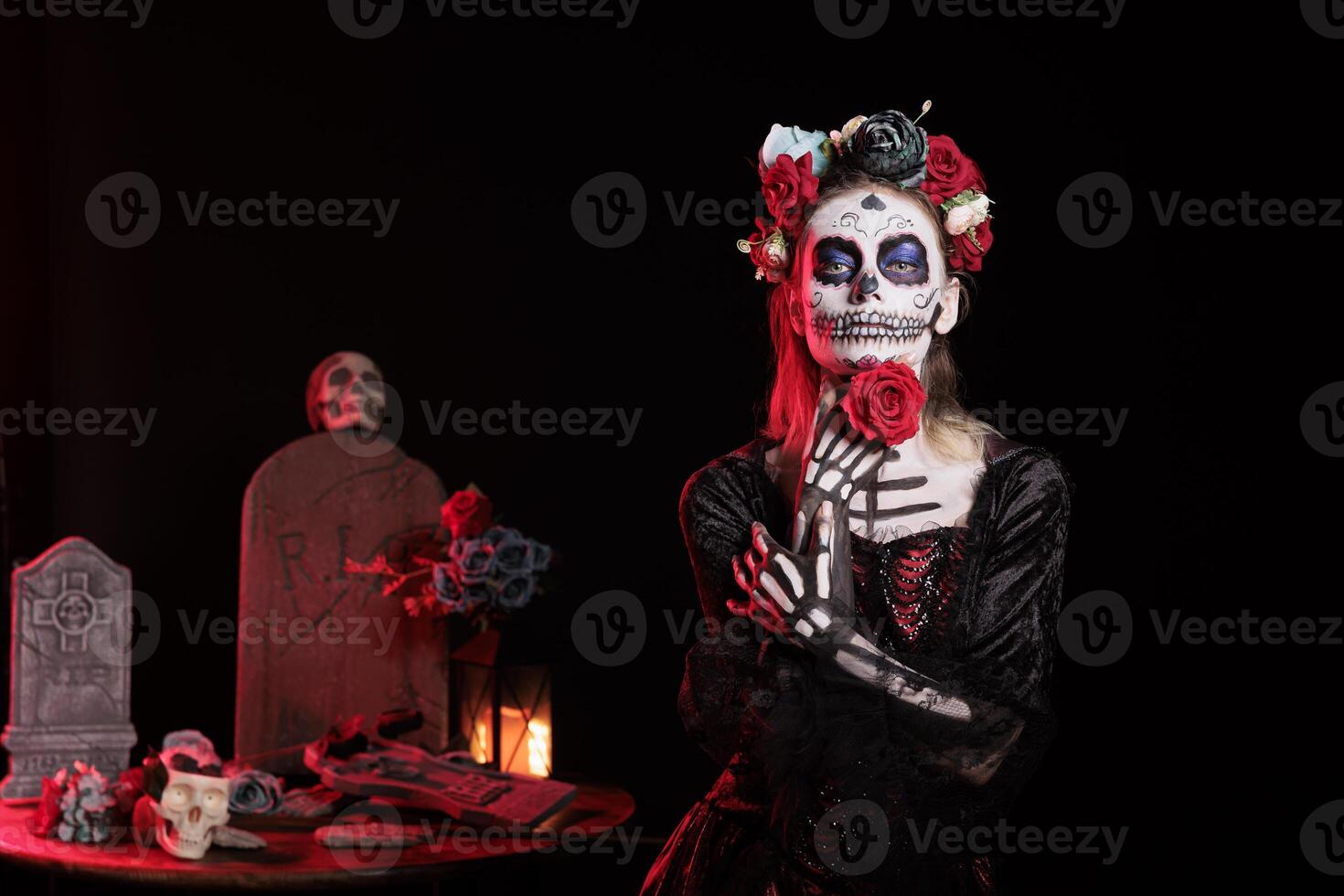 Dark lady posing with red rose during Day of the Dead event, preserving cultural traditions between generations. Woman wearing la Catrina costume and skull face paint to celebrate Mexican culture photo