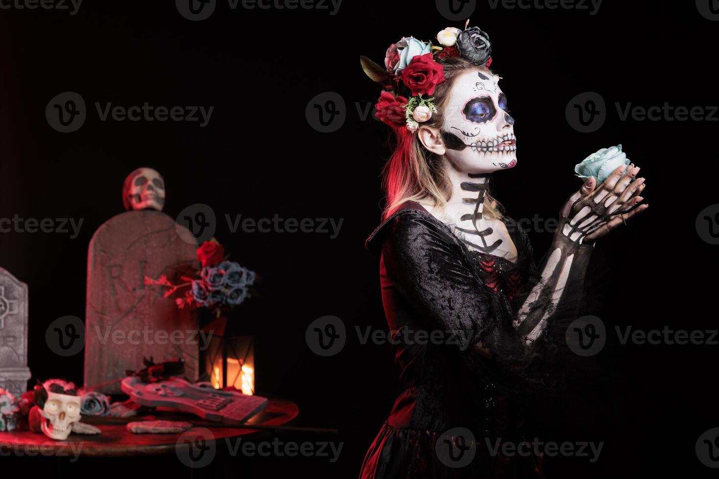 Woman gifting blue rose to dead relatives in graveyard, celebrating Dia de los Muertos. Mysterious lady with flower surrounded by frightening funeral items during Halloween horror event photo