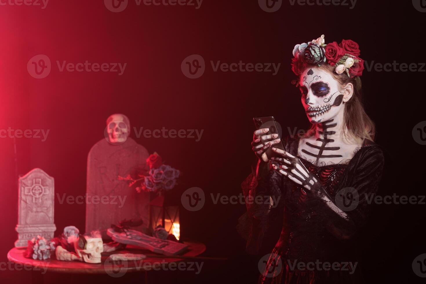 Woman holding mobile phone at Day of the Dead event to remember the deceased, celebrating their memory. Lady texting on smartphone during Mexican holiday of remembrance for those who have passed photo
