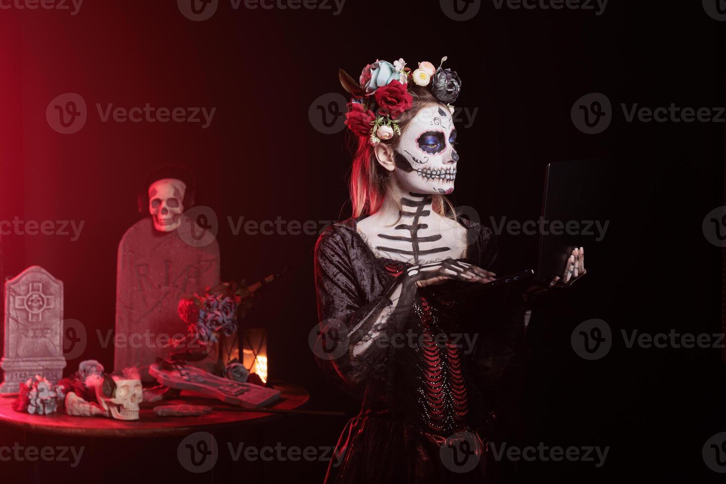 Woman working on laptop during Day of the Dead Mexican event honoring dead loved ones. Person sending emails on notebook during Halloween ancient Aztec custom of celebrating ancestors event in office photo