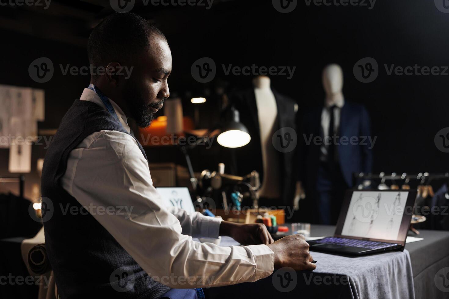 Experienced couturier stiching together bespoken business suit, looking online for inspiration. Skilled suitmaker working in tailoring studio, creating stylish custom made sartorial garment photo