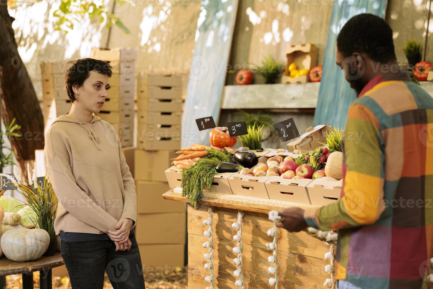 Multicultural customers standing near greenmarket booth, looking at seasonal homegrown food products. Young black man and caucasian woman shopping for healthy produce, fresh fruits and veggies. photo