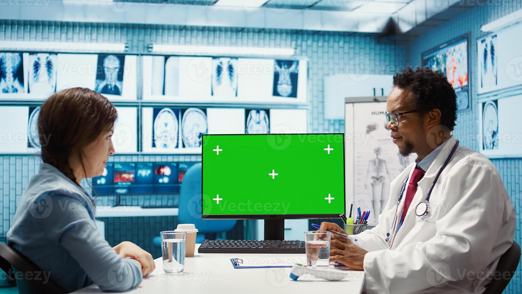 General practitioner consulting a female patient next to isolated chroma key display, sharing insight on lab test results and analysis. Skilled medic supports his client, indoors check up. Camera B. photo