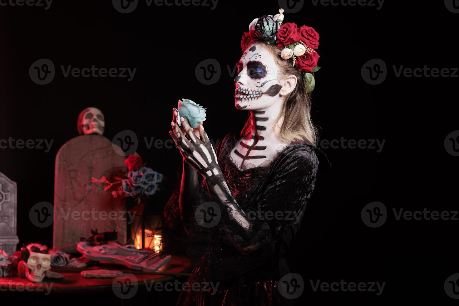 Person with blue rose at religious processions during Dia de los Muertos november holiday. Woman wearing skull face paint and floral wreath symbolizing reverence for the deceased, studio background photo
